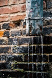 Water flows from a weathered pipe on a rustic brick wall, capturing urban charm.