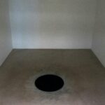 Abstract minimalist art piece featuring a black circle on a plain floor in a stark room.