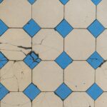 Top view of a cracked geometric tile pattern featuring blue diamond tiles on a beige background.