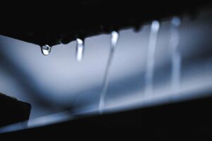 Closeup of water drops dripping and flowing down from dark surface in daylight