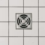 Top view of white ceramic tile floor with stainless steel square shaped cover of drain in contemporary shower