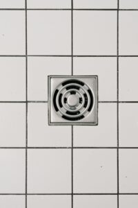 Top view of white ceramic tile floor with stainless steel square shaped cover of drain in contemporary shower