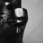 Minimalist black and white photo of a drop of water hanging from a faucet.
