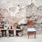 A rustic outdoor scene featuring a chair and potted plants against a weathered wall.